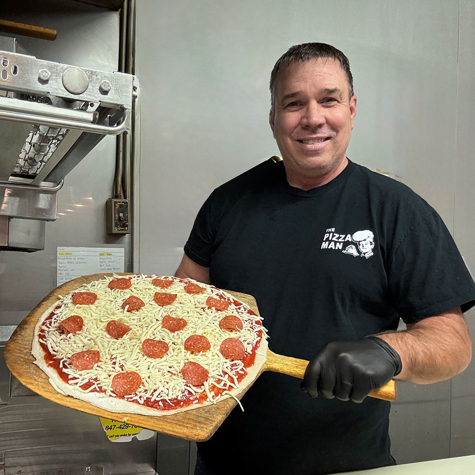 Owner Greg Addis holding holding up a pizza on a board